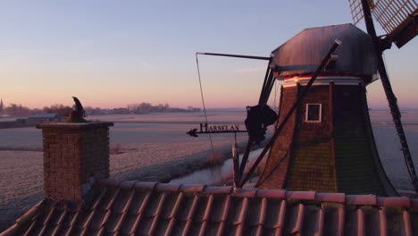 Shot-of-a-wind-vane-next-to-a-dutch-windmill-Babuurstermolen-during-sunrise,-aerial