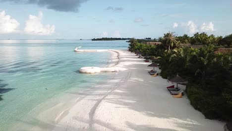 Drone-flying-above-Maldives-Island-sea-shore,-blue-water,-white-sand,-green-palms-and-villas