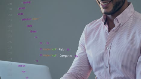 animation of multicolored computer language over smiling biracial man working on laptop