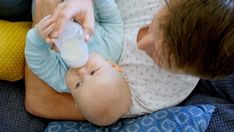 Vater-Füttert-Seinen-Kleinen-Jungen-Im-Wohnzimmer-Mit-Milch-4k