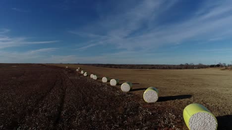 Weitläufige-Drohnenluftaufnahme-Einer-Baumwollfarm-Im-Mittleren-Westen-Mit-Frischen-Ballen-Geernteter-Baumwolle,-Die-In-Leuchtend-Gelbes-Material-Vor-Einem-Blauen-Himmel-Eingewickelt-Sind