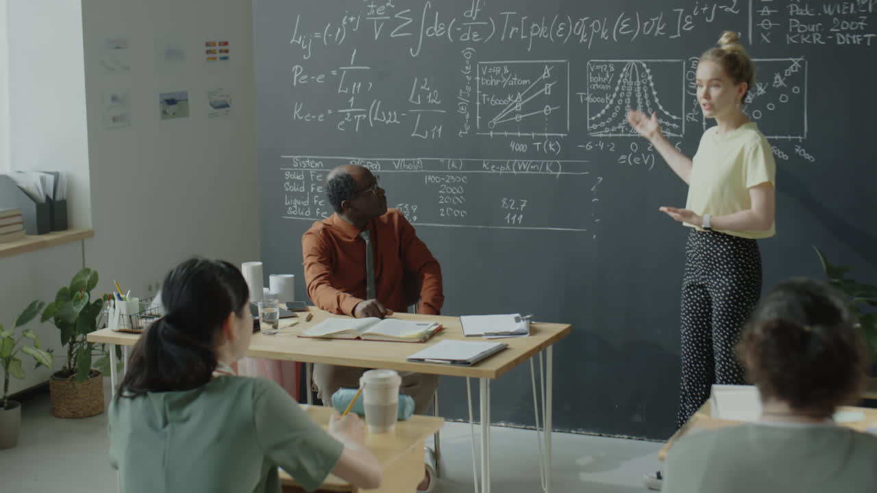 A female teacher presenting in a classroom with students and a male professor