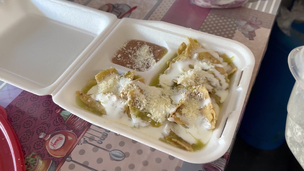 Håndholdt optagelse af en kvinde, der drysser cotija-ost over chips i en plastikbakke, klar til servering.