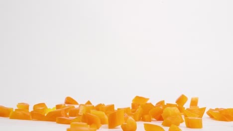 Diced,-cubed-bright-orange-bell-pepper-vegetable-pieces-falling-onto-white-table-top-and-bouncing-into-a-pile-in-slow-motion