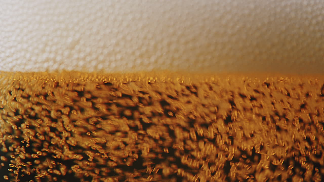 Macro shot of pouring beer with bubbles and foam into a glass