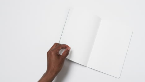 Video-of-hand-of-african-american-man-holding-book-with-blank-pages,-copy-space-on-white-background