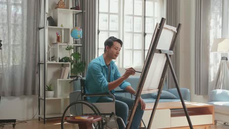side view of an asian artist man in wheelchair holding paintbrush mixed colour and thinking before painting on the canvas