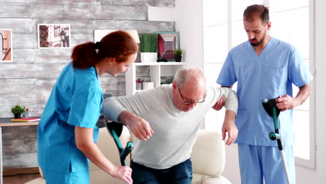 Old-man-with-crutches-helpd-by-young-male-doctor-and-woman