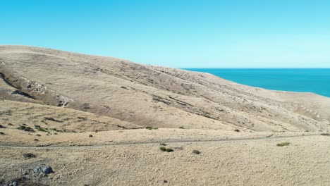 Flying-sideways-parallel-to-gravel-road-as-barren-peninsula-hills-drop-away-to-ocean---Banks-Peninsula-South