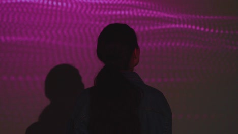silueta de una mujer visitando una exposición de arte inmersiva con proyección de formas en la pared