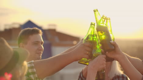 russian people clinks glasses and drinks beer from green bottels on the party with friends on the roof