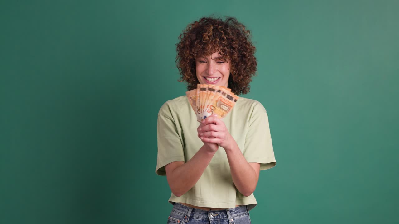 Cheerful woman showing Euro banknotes in green studio