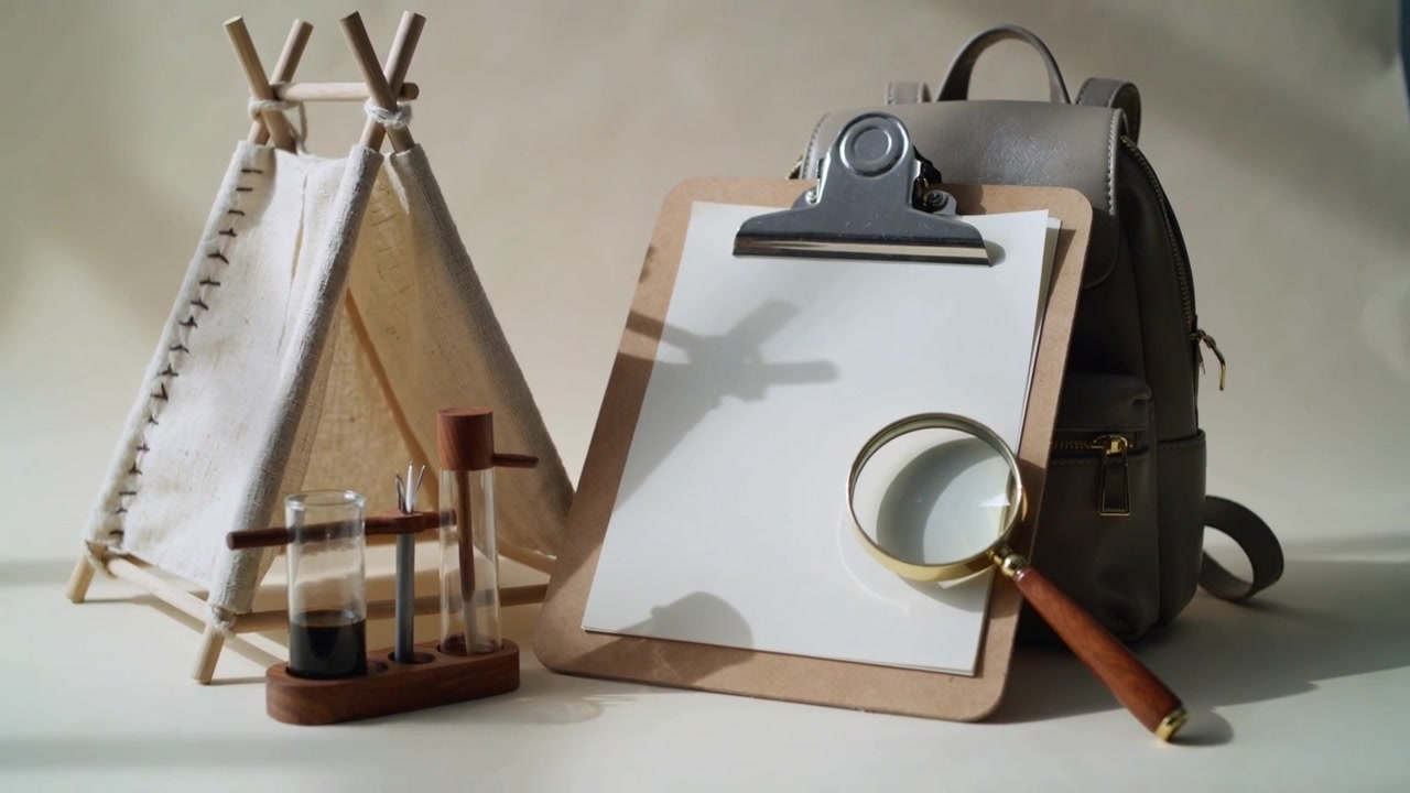 Shifting camera to center clipboard holding blank sheet and magnifier on table, teepee and backpack