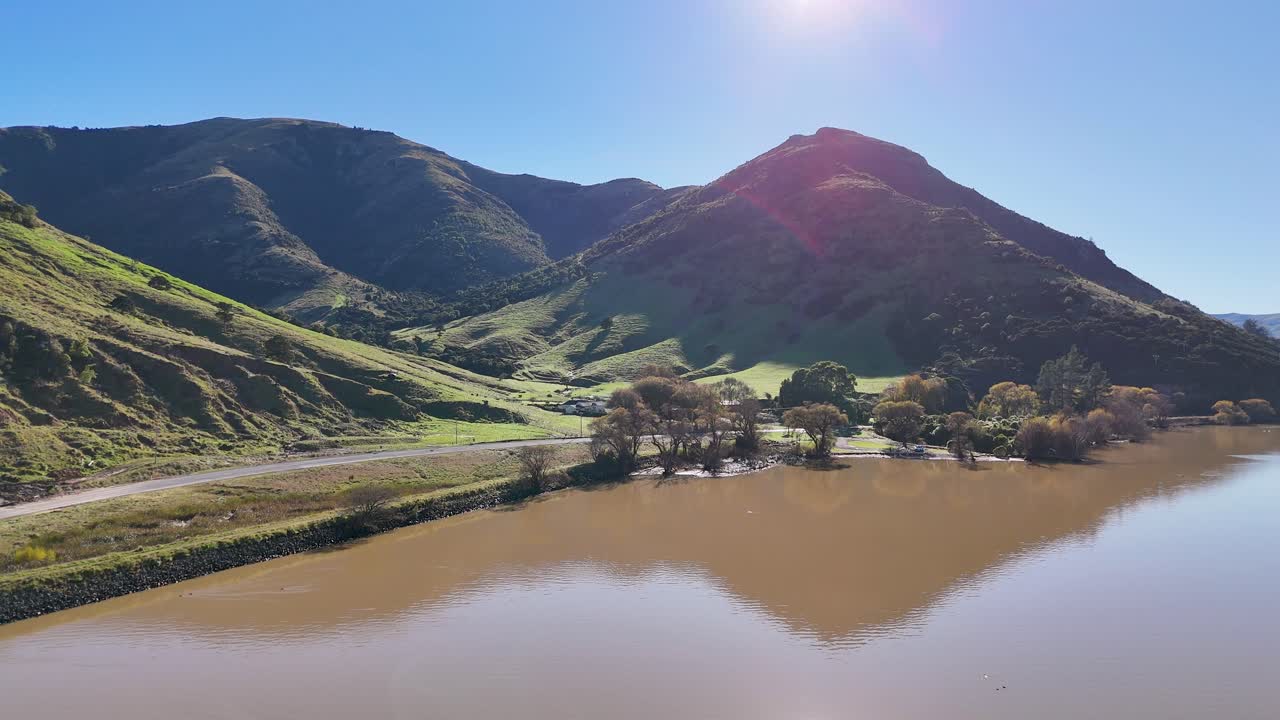 A tranquil scene of Akaroa's hills and reflective lake under bright sunlight, showcasing natural beauty and calmness