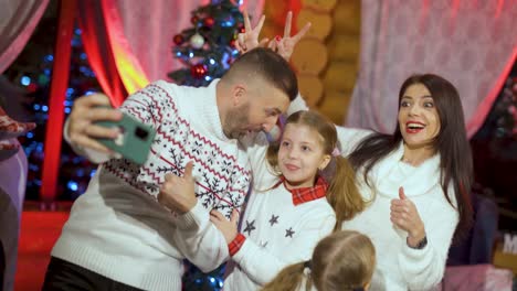 Happy young couple with small children near glowing bright decorated Christmas Tree using smartphone take photography capture moment New Year celebration, family having fun on xmas eve concept