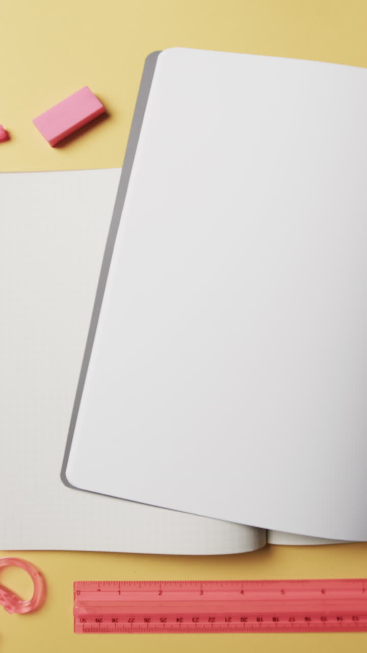 Vertical video of overhead view of open notebooks on beige background, in slow motion