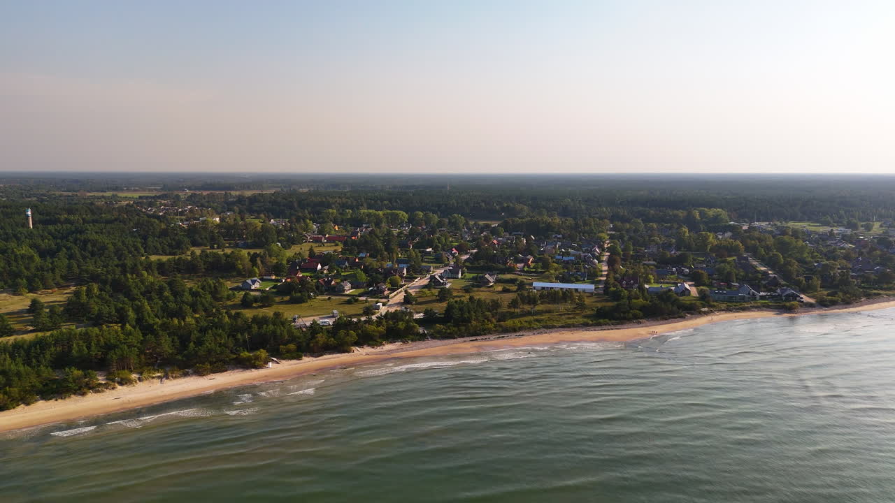 라트비아의 파빌로스타의 드론 영상입니다. 해안선, 모래 해변, 마을을 보여줍니다.