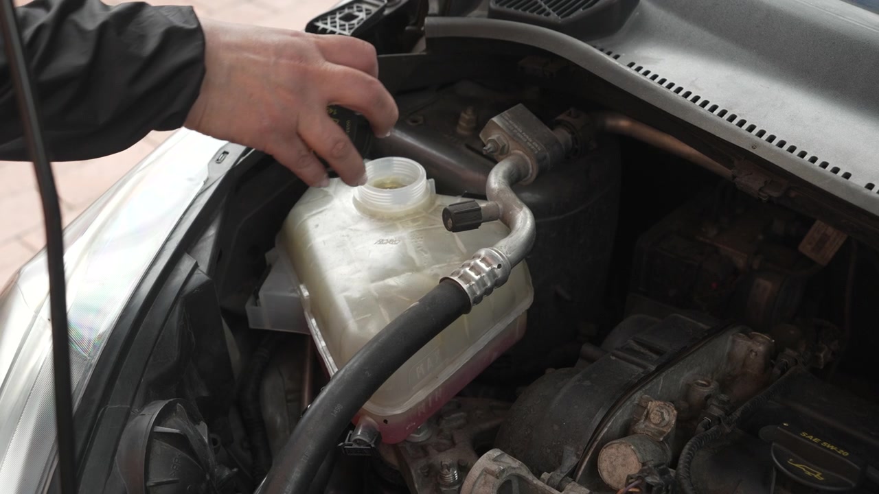 Professional mechanic checking the coolant level by unscrewing the expansion tank cap under the hood