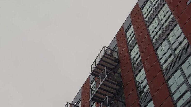 Panorâmica lenta e constante para baixo, revelando varandas empilhadas em um prédio de apartamentos urbano moderno