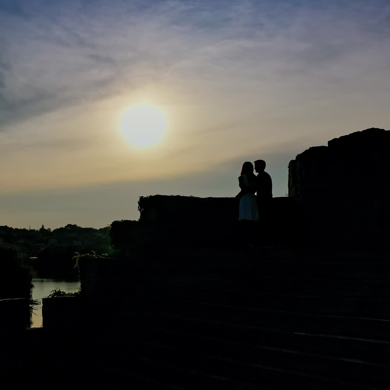 Romantic couple in love spending time together at sunset. Young man kisses girlfriend standing in a castle over the water in the evening.