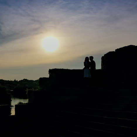 Romantic couple in love spending time together at sunset. Young man kisses girlfriend standing in a castle over the water in the evening.