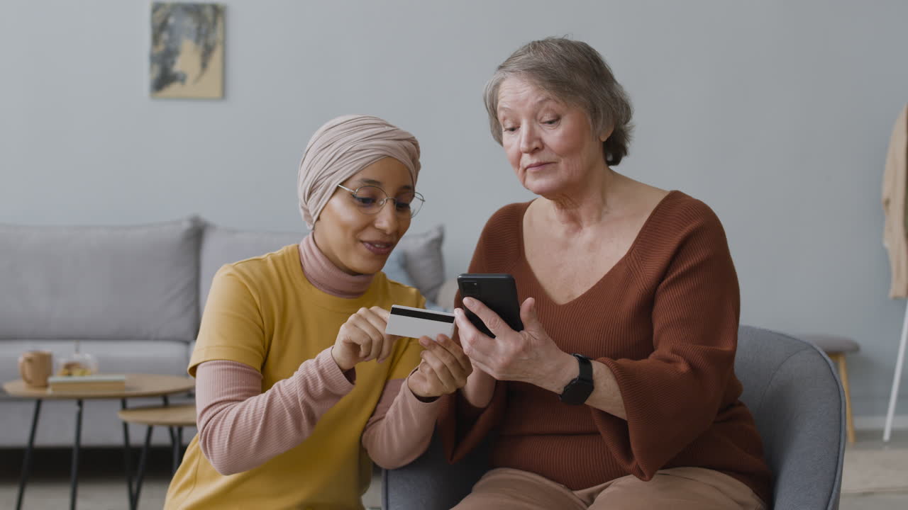 Arabic Woman Teaching An Elderly Woman To Use Mobile Payment With Credit Card 3