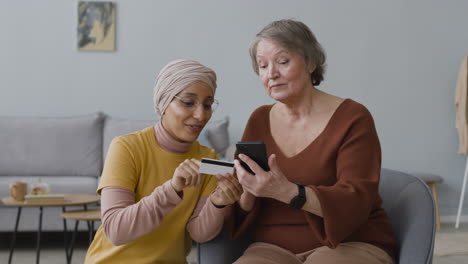 Mujer-árabe-Enseñando-A-Una-Anciana-A-Usar-El-Pago-Móvil-Con-Tarjeta-De-Crédito-3