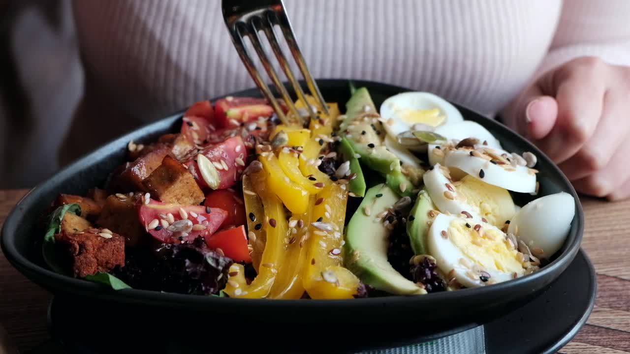 Close up of a woman eating a salad in a black bowl at a restaurant