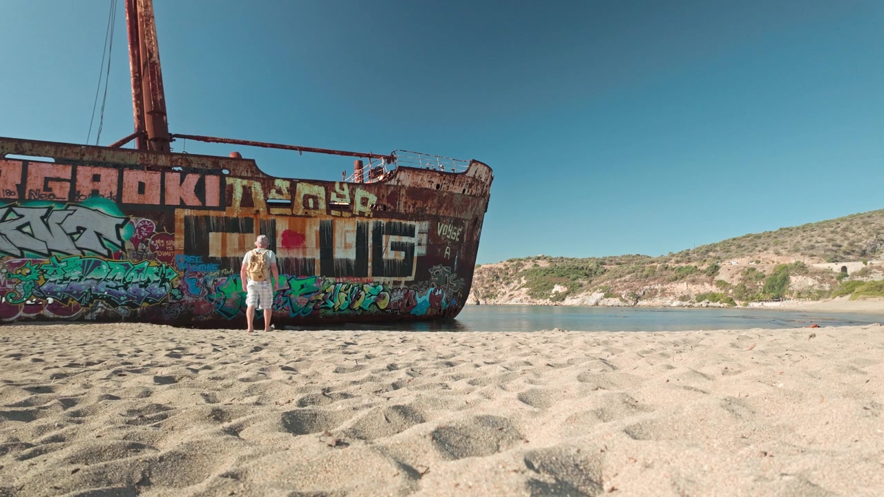Meraklı sahil gezgini, paslı, çürüyen bir Yunan gemi enkazındaki grafitiyi izliyor.