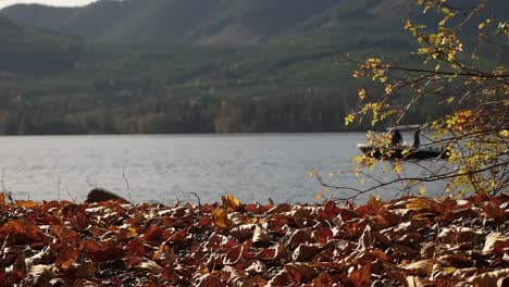 Kleines-Fischerboot-Auf-See-Unscharf-Mit-Vordergrund-Der-Roten-Herbstblätter-Und-Busch-Im-Fokus