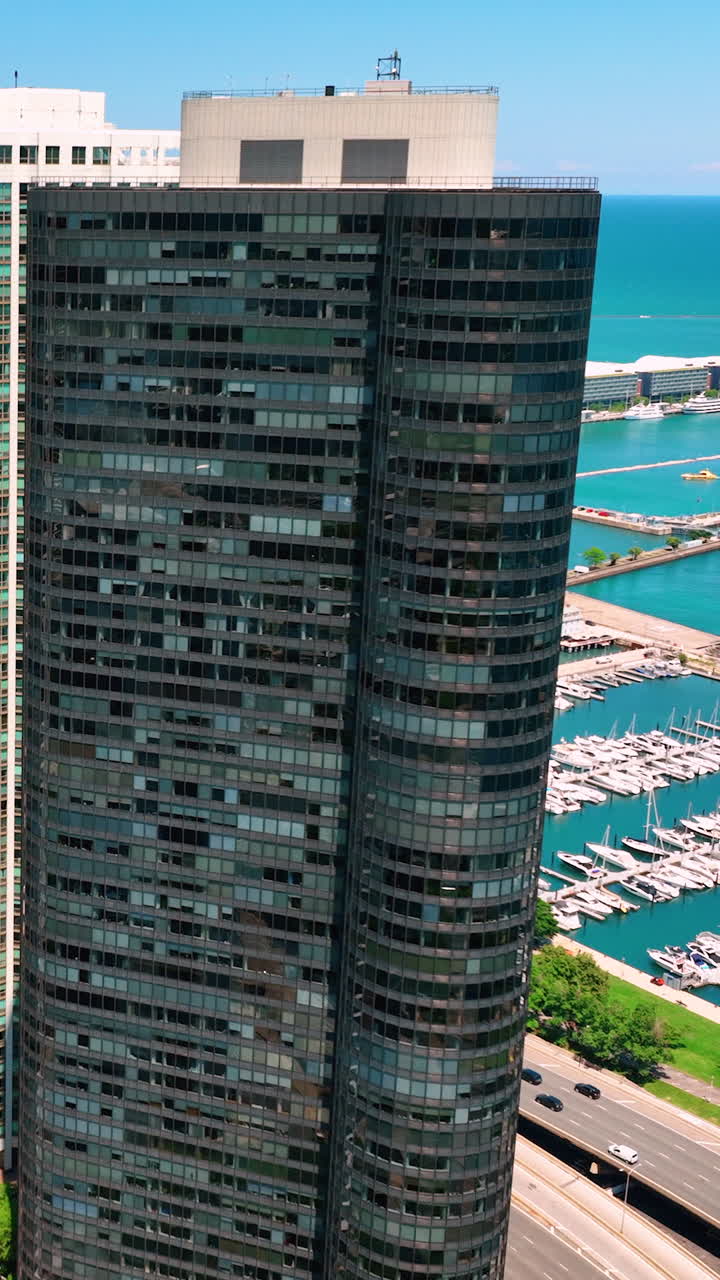 A tall glass dark skyscraper on the shore of a lake with parked boats and yachts. Aerial view of downtown Chicago. DuSable Harbor. Vertical video