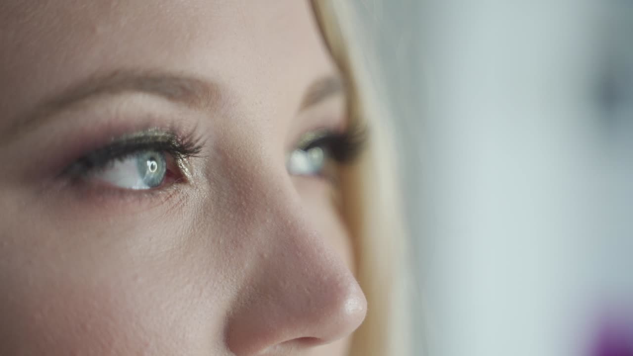 Sensitive, dreamy, sad and thoughtful blue eyes of blond women looking out of window - cinematic close up macro shot