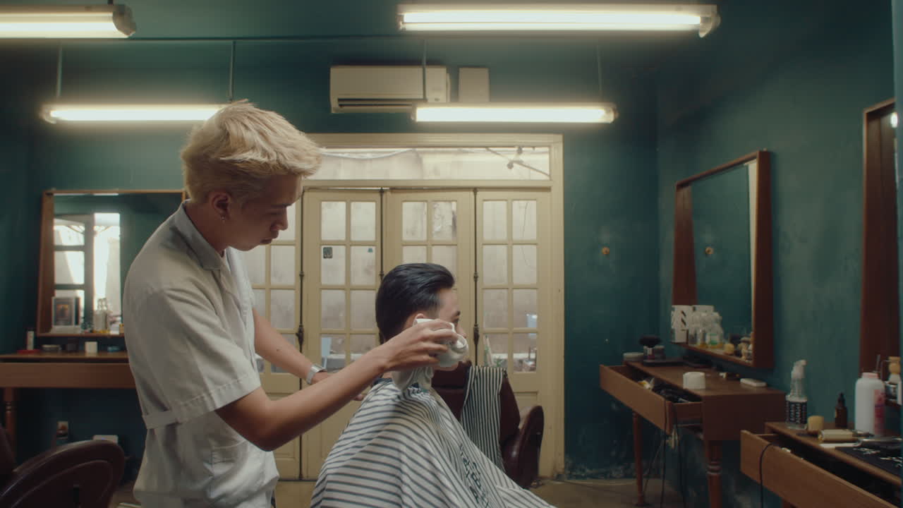 Asiatisk barber renser mandlig kundes nakke med et håndklæde