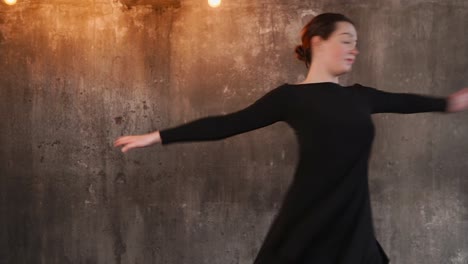 woman dancing in a black dress against a concrete wall