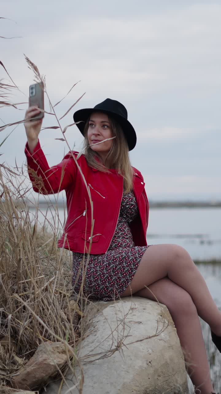 Donna che si fa un selfie con una giacca di pelle rossa e un cappello nero