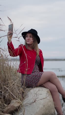 Woman taking a selfie in a red leather jacket and black hat