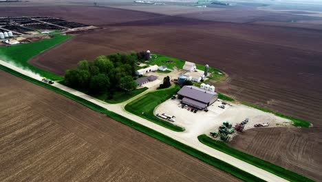 Aerial-drone-footage-of-a-tractor-and-planter-going-down-a-gravel-road-pulling-into-a-farm