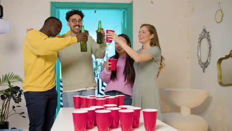 happy multiethnic young friends toasting with beer at home