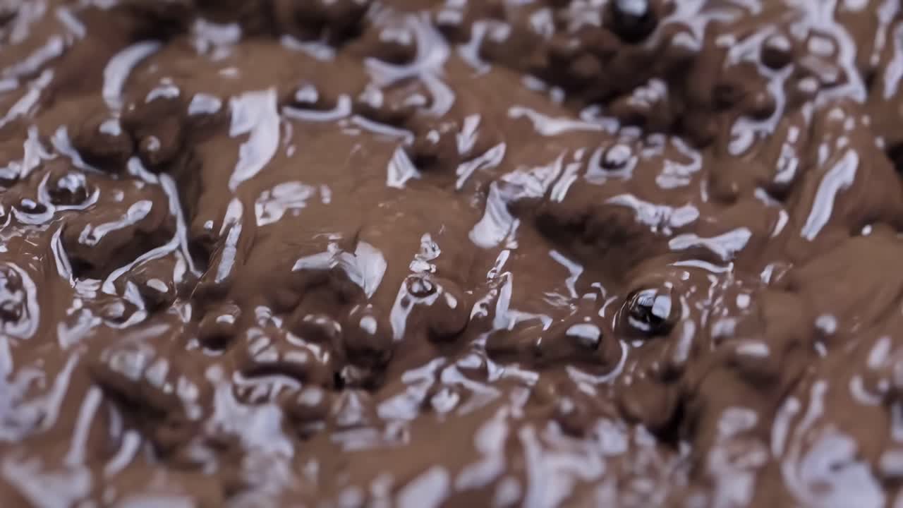 Close-up video of bubbling chocolate sauce, shot from above. The rich texture and glossy surface