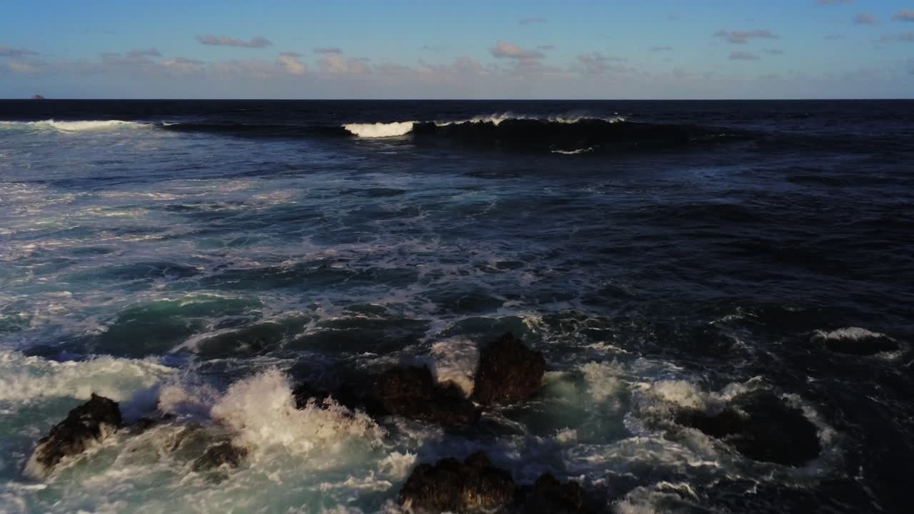 Costa rocciosa bassa con onde oceaniche che si infrangono e schizzano, vista aerea a bassa quota.
