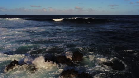 Shallow-rocky-coastline-with-ocean-waves-breaking-and-splashing,-low-altitude-aerial-view