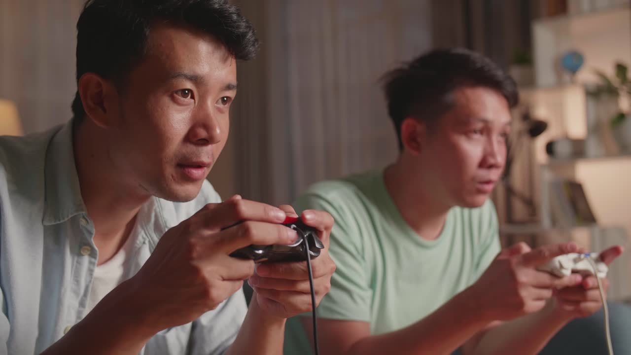 Asian Friends Playing Video Games At Home. Male Happy To Win Victory And Another Man Feeling Disappointed