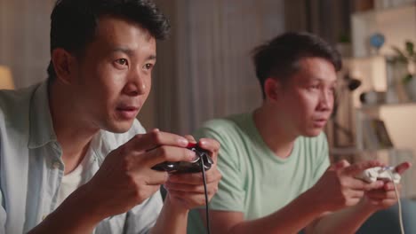 Asian Friends Playing Video Games At Home. Male Happy To Win Victory And Another Man Feeling Disappointed
