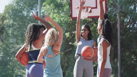 Happy-diverse-female-basketball-team-training-on-sunny-court,-in-slow-motion