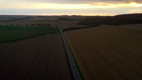 aerial drone shot over a rural road between fields of ripe corn during evening time