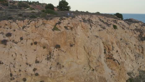 Luftaufnahmen-Eines-Mannes,-Der-Eine-Drohne-Auf-Einer-Hohen-Klippe-Mit-Blick-Auf-Eine-Küstenstraße-Und-Einen-Bootssteg-Am-Meer-Bedient