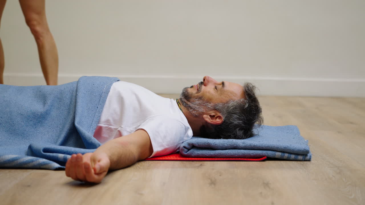 Hombre descansando en postura Savasana cubierto con una manta