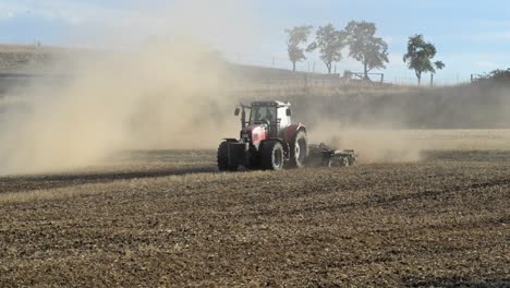 red tractor turning while plowing a dry dusty field to prepare it for sowing