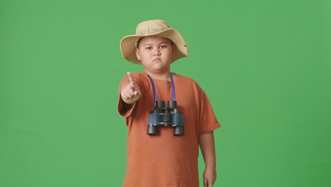 모자와 안경을 입은 아시아 관광 소년은 손가락을 당신 쪽으로 가리키고 머리를 흔들며 지표손가락을 흔들며 녹색 화면 배경에서 제안하는 것을 피합니다. 소년 연구자는 제스처를 표시하지 않습니다.