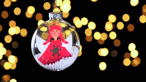 adorno de bola de navidad claro único con ángel de pelo rojo de dibujos animados y nieve dentro de las luces desenfocadas parpadeando en el fondo, cerrar